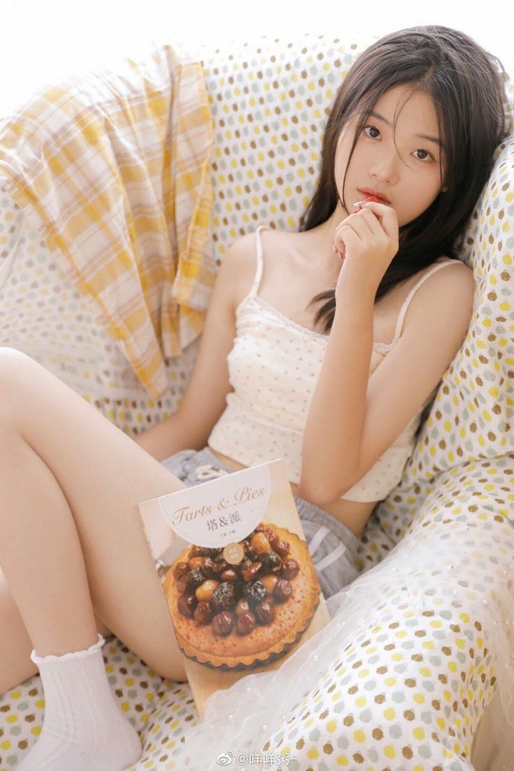 Young woman with long dark hair in a white camisole and shorts, holding a book