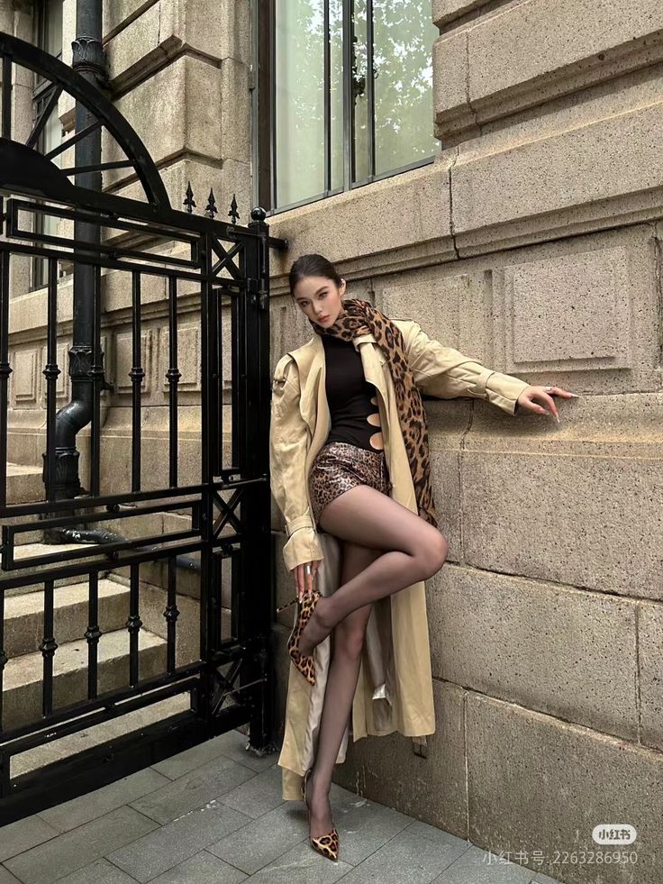 Woman in a trench coat, leopard print shorts, and black tights posing outdoors