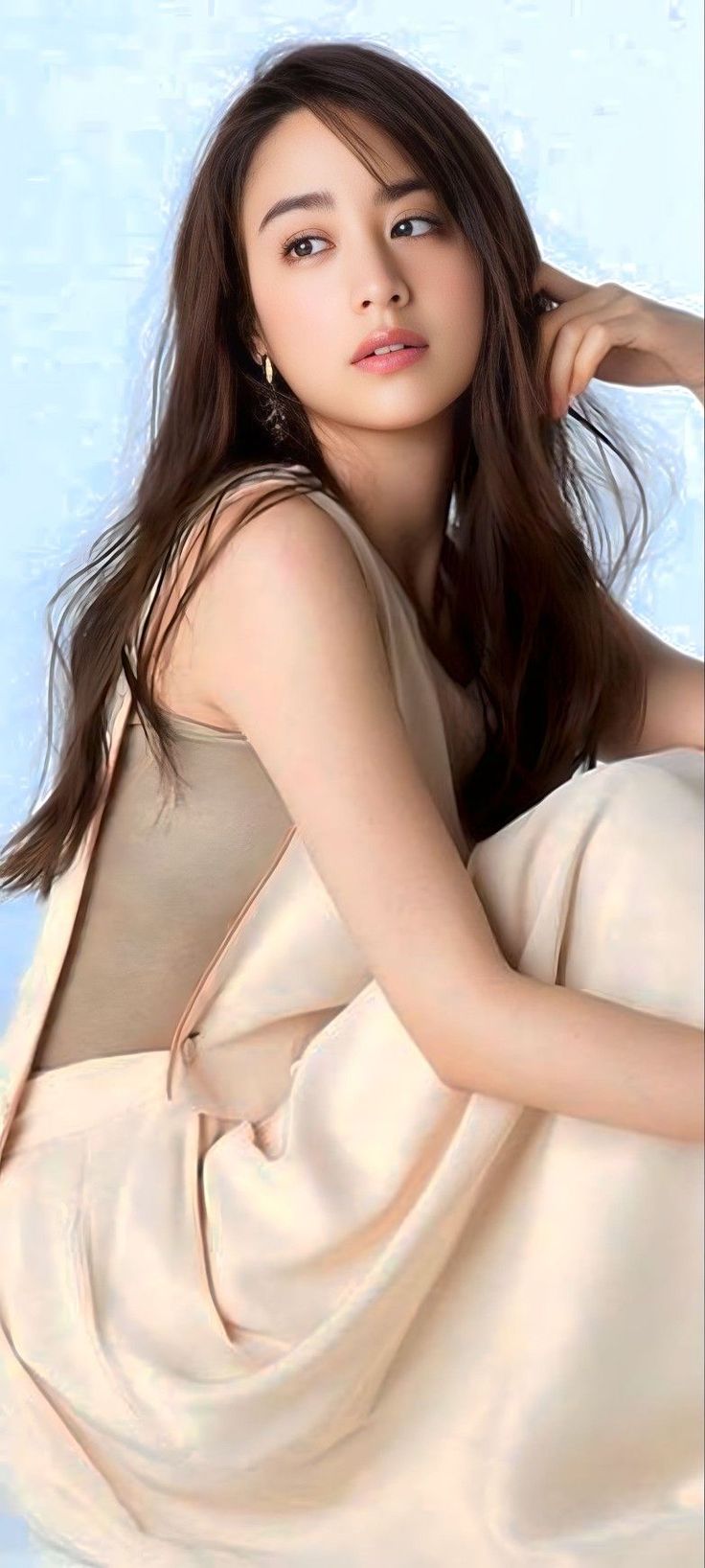 Woman with long brown hair and earrings against a light blue background