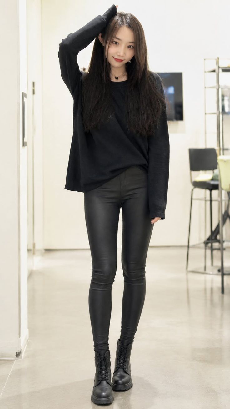 Woman with long dark hair wearing a black top and leather pants indoors