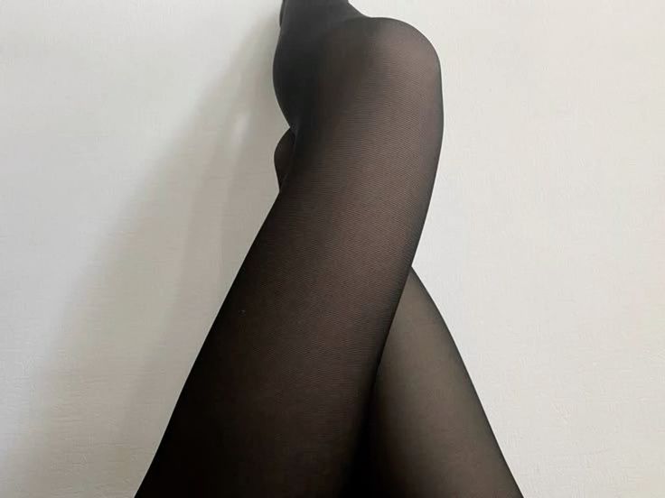 Person wearing black tights with legs crossed against a white background