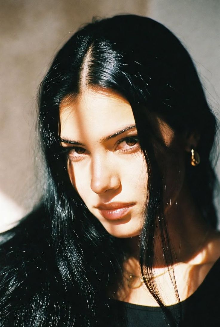 Woman with long black hair in dramatic lighting with shadows across her face