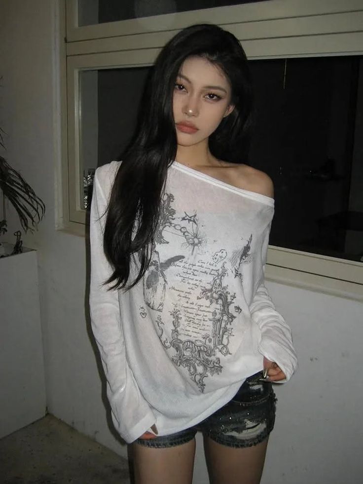 Woman with long black hair wearing an off-shoulder top and distressed shorts indoors