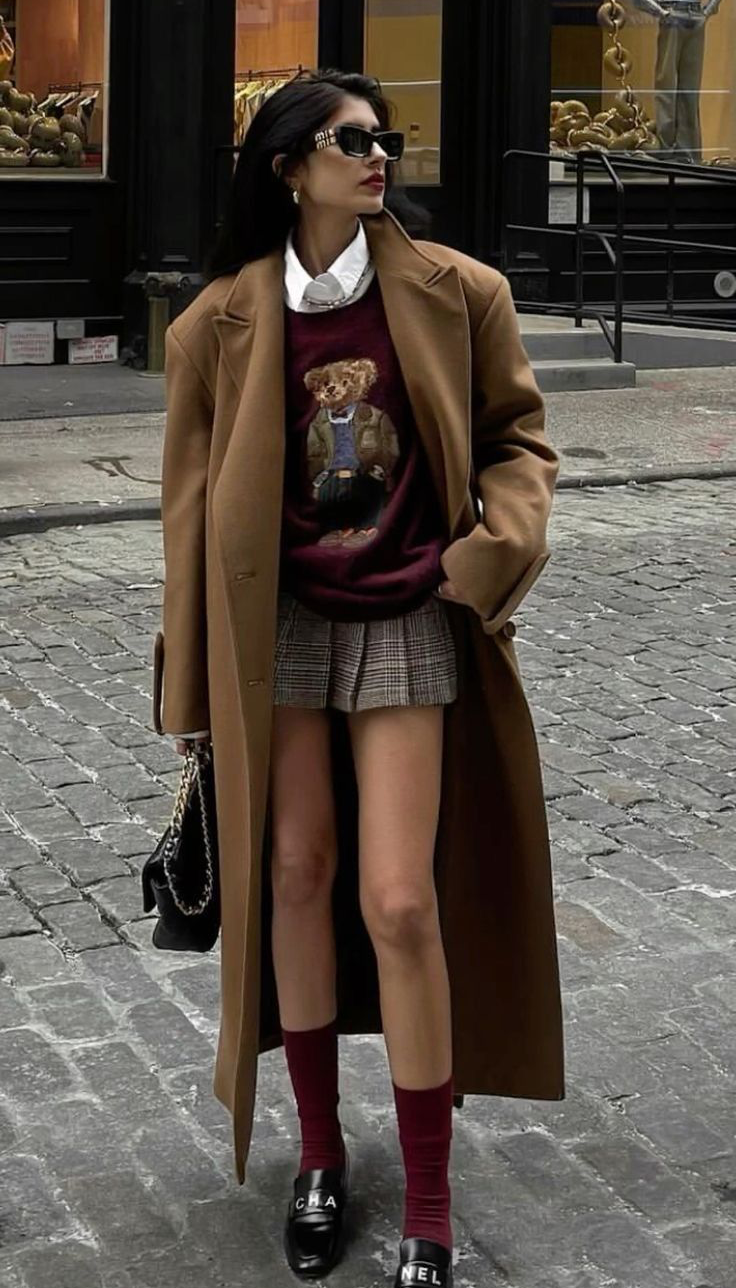 Woman in a long brown coat and plaid skirt on a cobblestone street