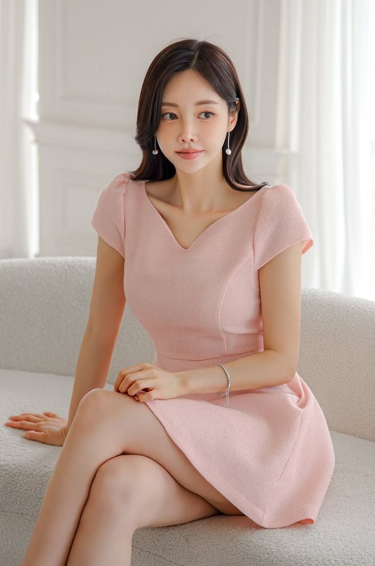 Woman in a pink dress and pearl earrings sitting on a sofa indoors