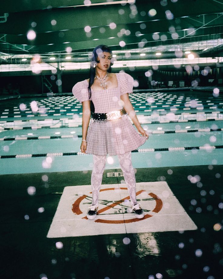Person in a plaid dress with puffy sleeves and a choker standing by a swimming pool