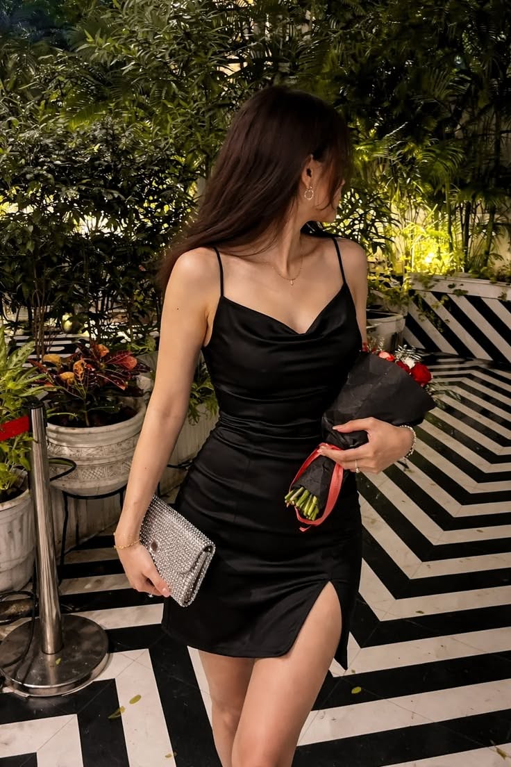 Woman in a black dress holding a sparkly clutch and red roses indoors