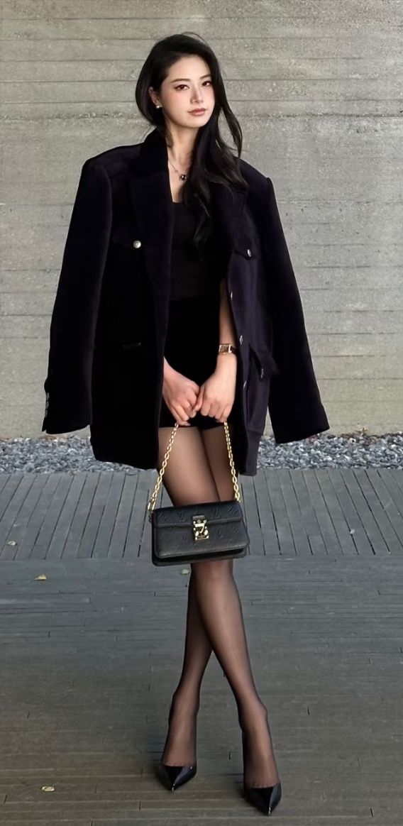 Woman in a black blazer and dress with a shoulder bag standing outdoors