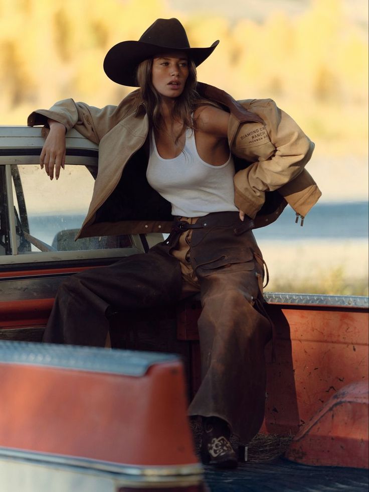 Woman in a cowboy hat and chaps leaning on a truck bed outdoors