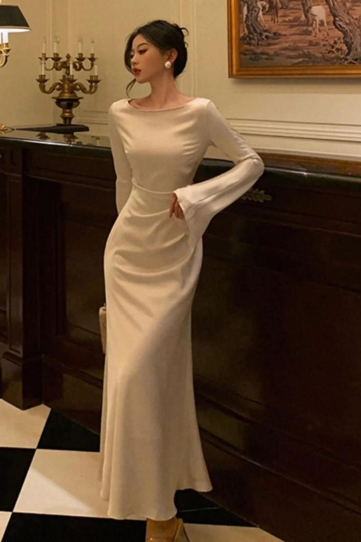 Woman in a long, elegant dress with long sleeves and pearl earrings indoors