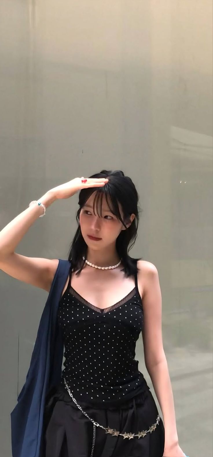 Woman with black hair wearing a polka dot top and pearl necklace outdoors