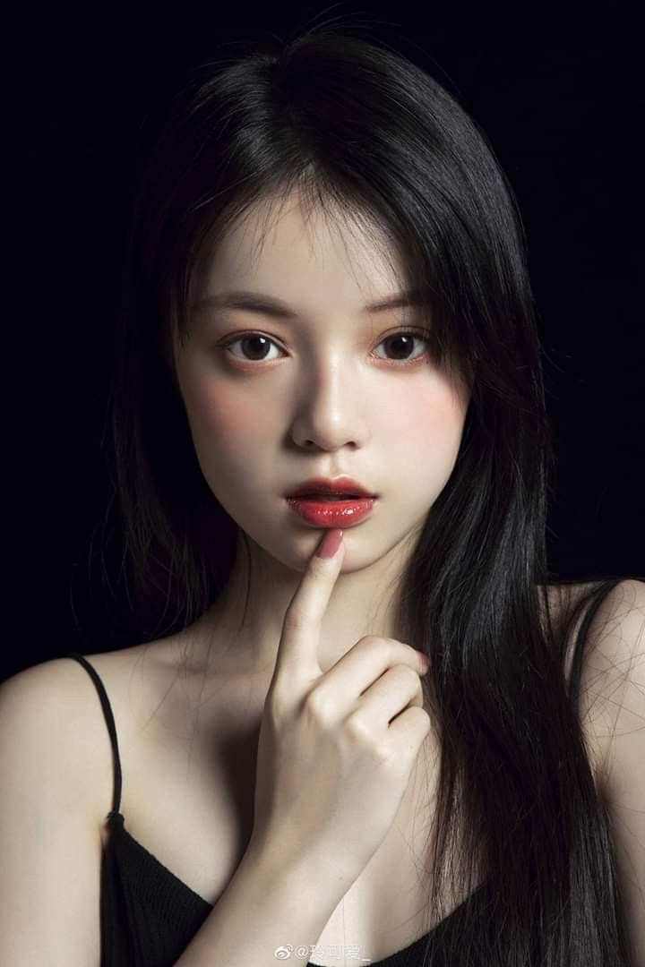 Woman with long black hair and red lipstick in a black top against a dark background