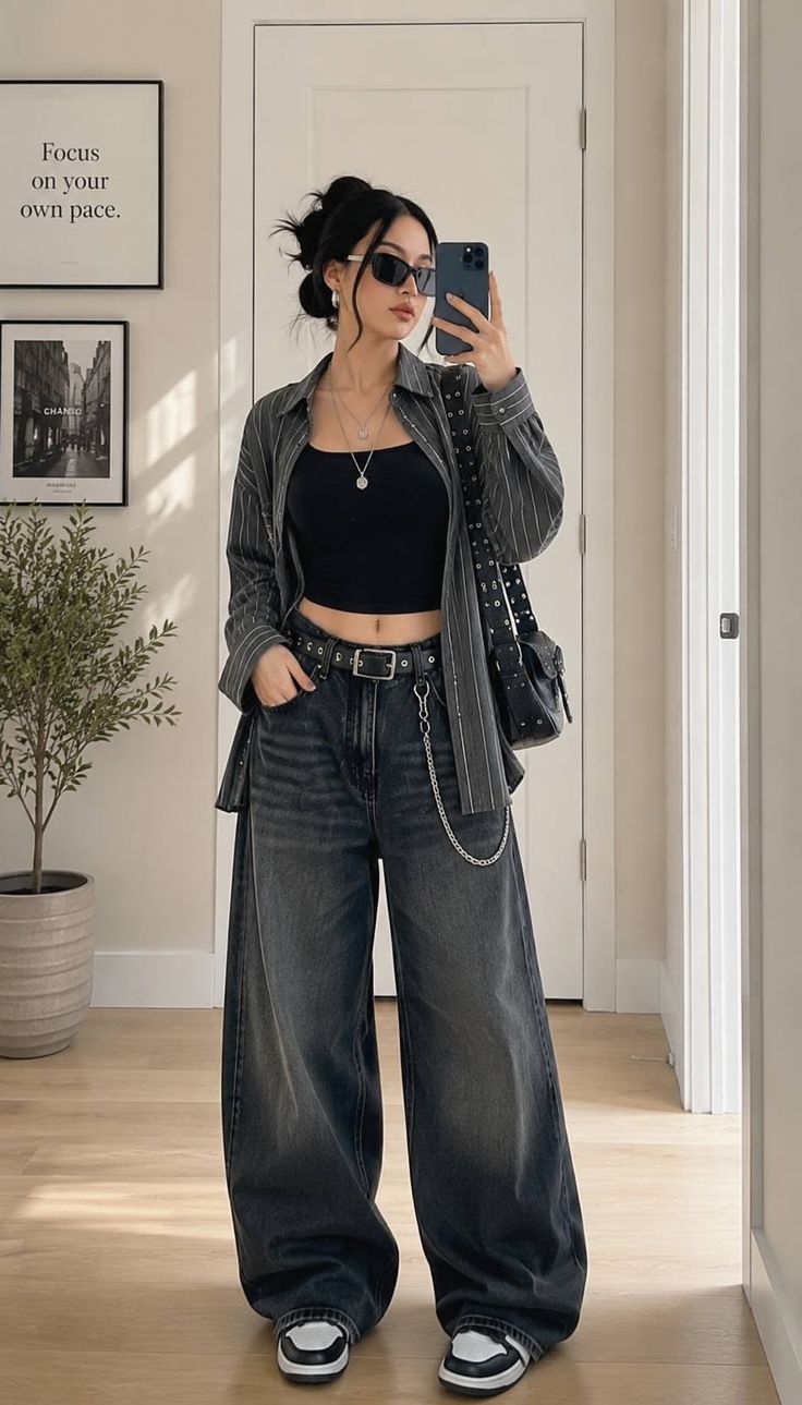 Woman in a black crop top and baggy jeans taking a mirror selfie