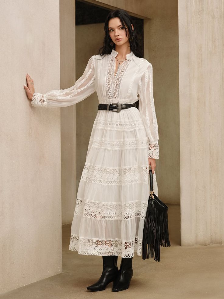 Woman in a white lace dress with a black belt and fringe bag indoors