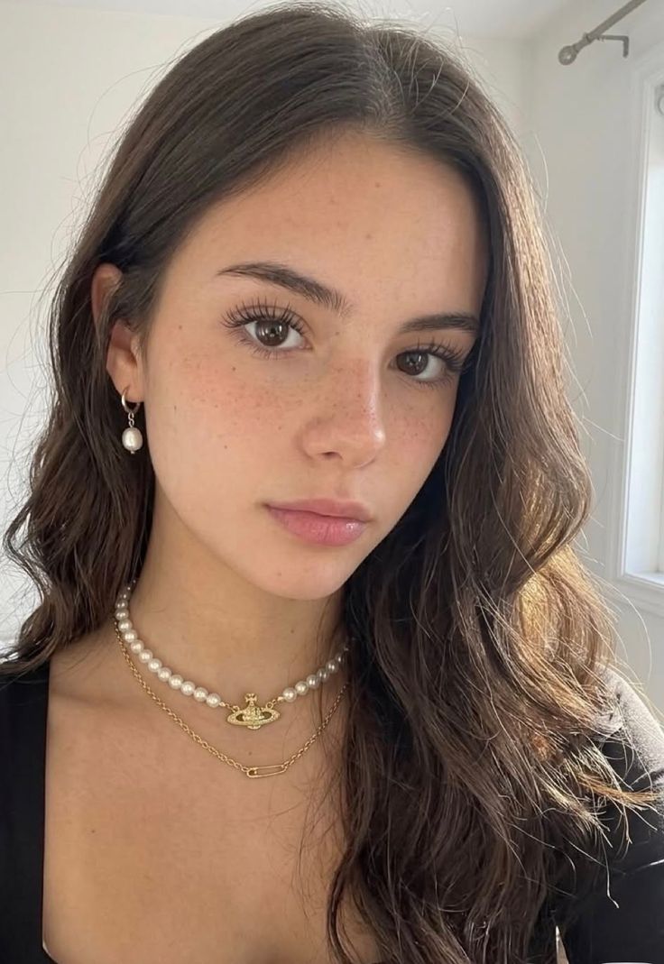 Woman with long brown hair and freckles wearing pearl jewelry indoors