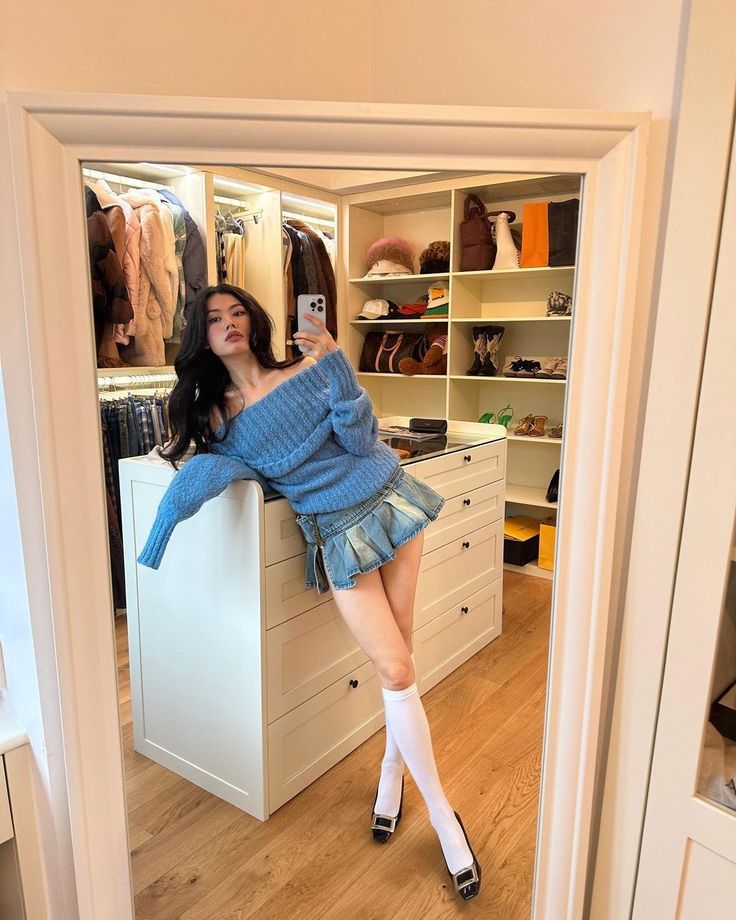 Woman in a blue sweater and denim skirt posing in a mirror selfie