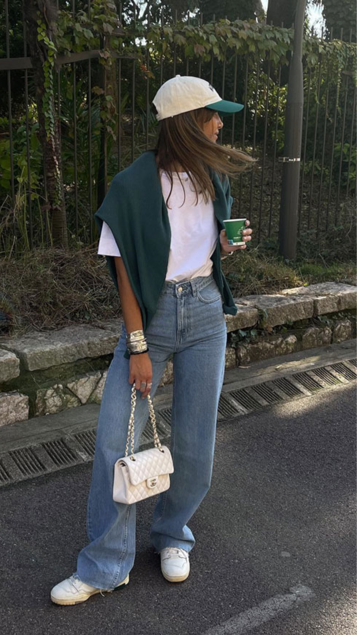 Woman in a baseball cap and wide leg jeans holding a coffee cup and handbag outdoors