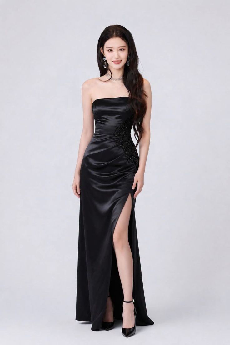 Woman in a black strapless dress with a high slit and jewelry posing in a studio