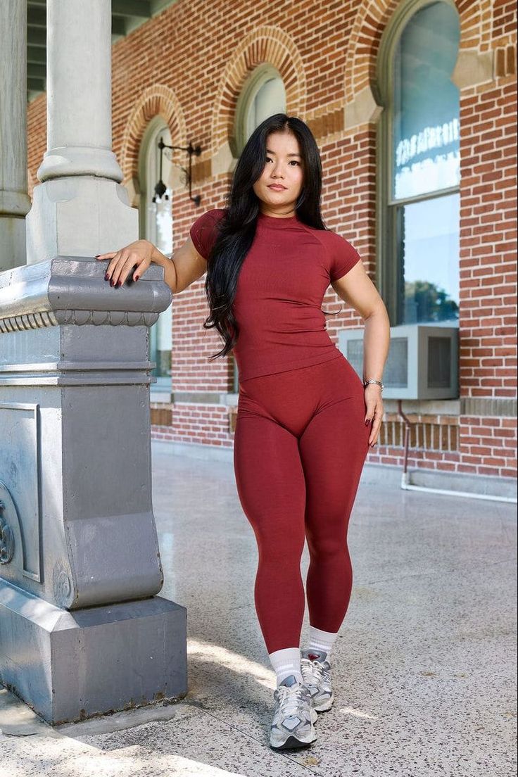 Woman in a red athletic outfit posing outdoors next to a pillar