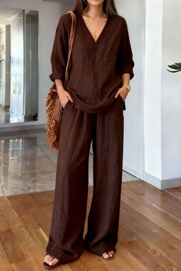 Woman in a brown linen top and wide leg pants with a straw bag indoors