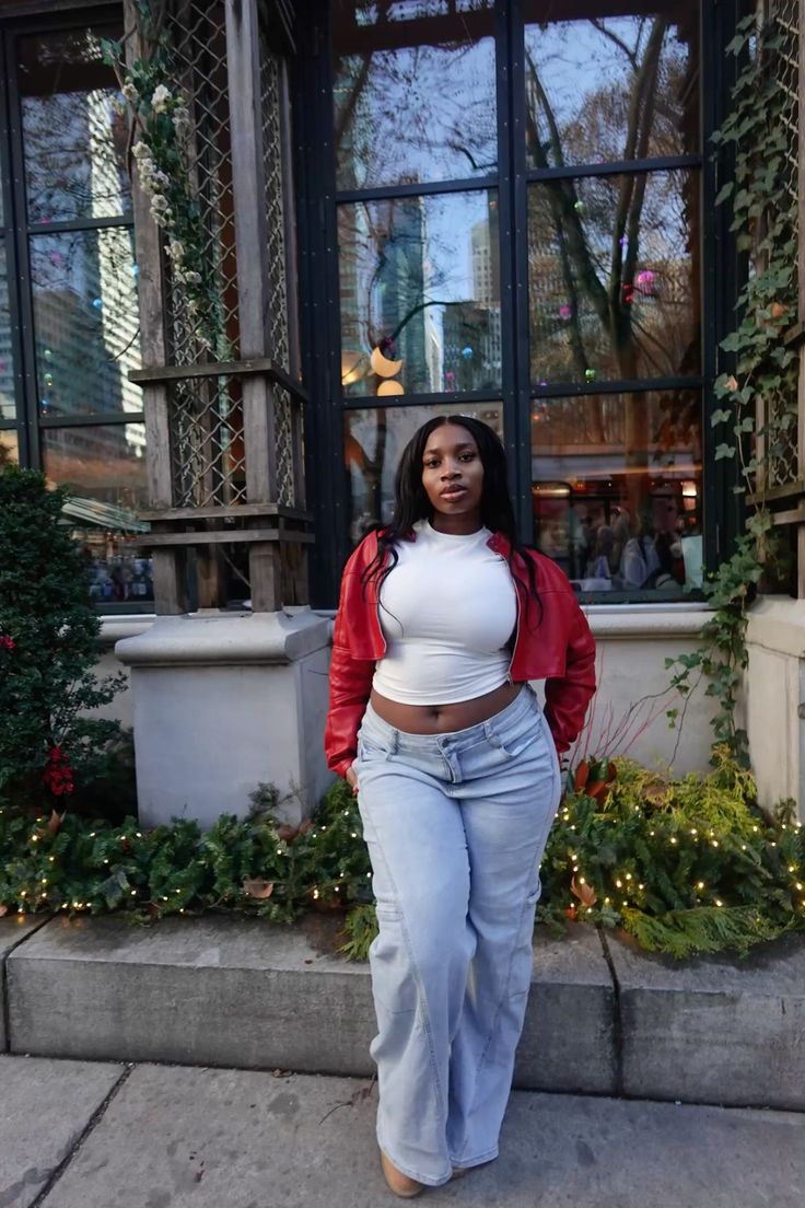 Woman in a red jacket and white crop top with light wash jeans outdoors