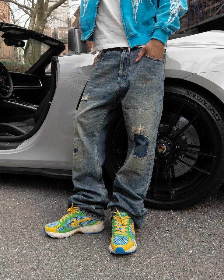 Person in distressed jeans and colorful sneakers leaning against a white sports car