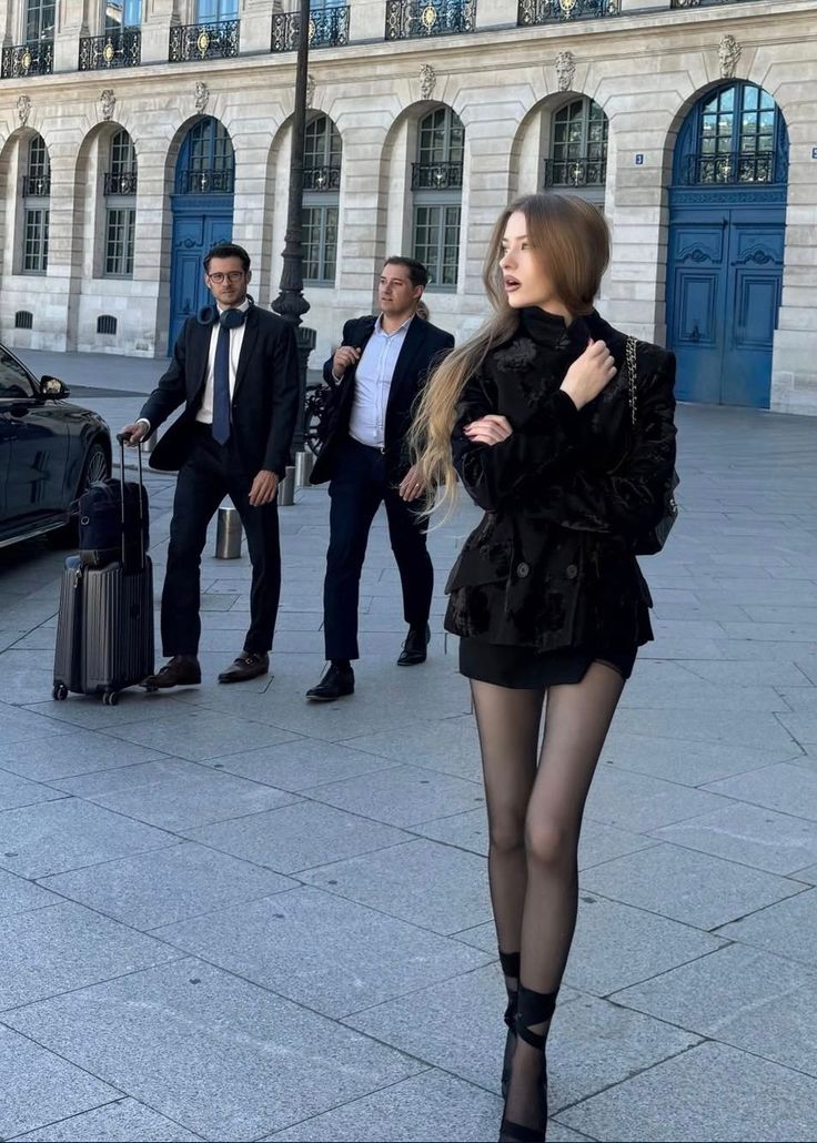 Woman in a black jacket and mini skirt walking on a street with two men