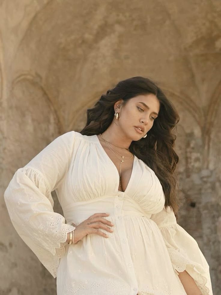 Woman with long dark hair in a white dress with cleavage and jewelry