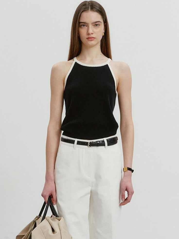 Woman in a black halter top and white pants holding a bag