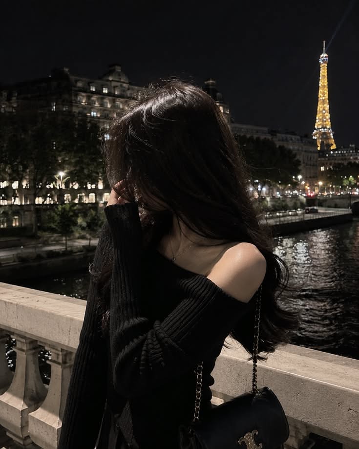 Woman with long dark hair on a bridge at night with the Eiffel Tower in the background