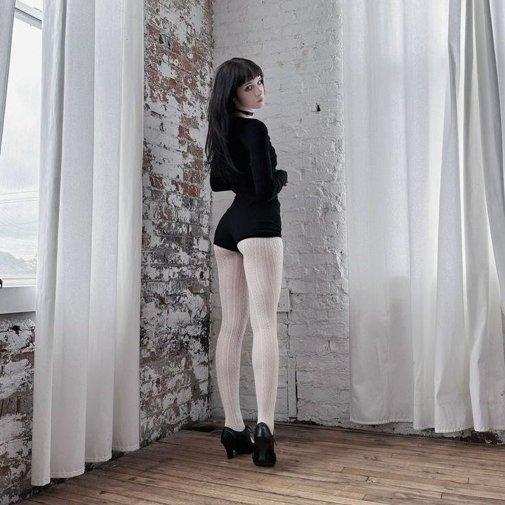 Woman in black shorts and white tights looking over her shoulder