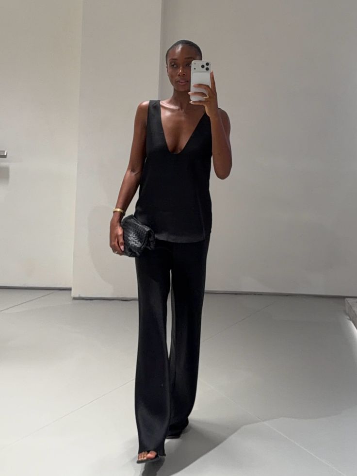 Woman in a black top and wide leg pants taking a mirror selfie