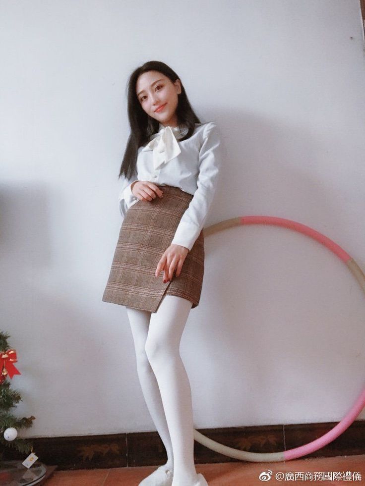Woman in a white blouse and plaid skirt with white tights indoors