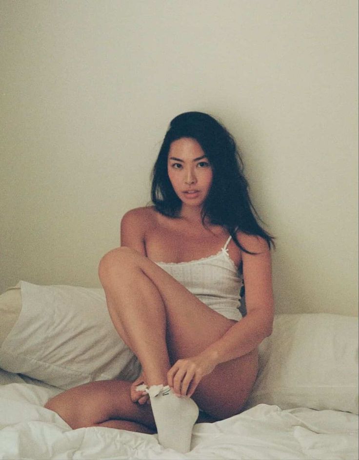 Woman in a white tank top and socks sitting on a bed