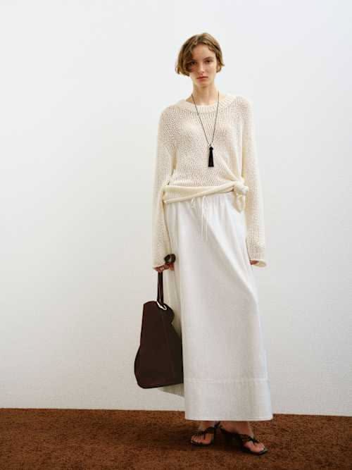 Woman in a white knit sweater and maxi skirt holding a brown bag
