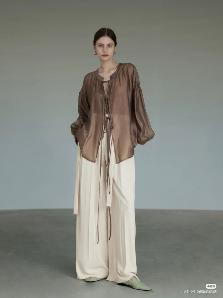 Woman in a sheer brown top and wide leg pants standing indoors