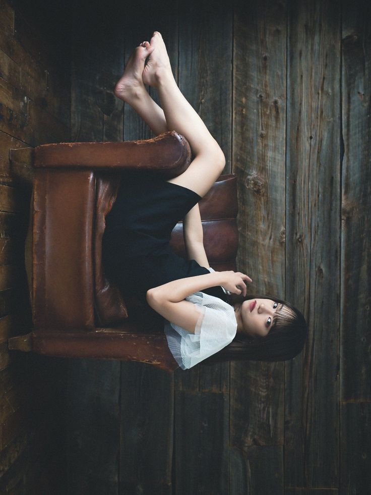 Woman in a black dress lying on a brown armchair with her feet up against a wooden wall