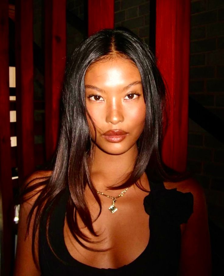 Woman with long black hair wearing a black top and necklace indoors
