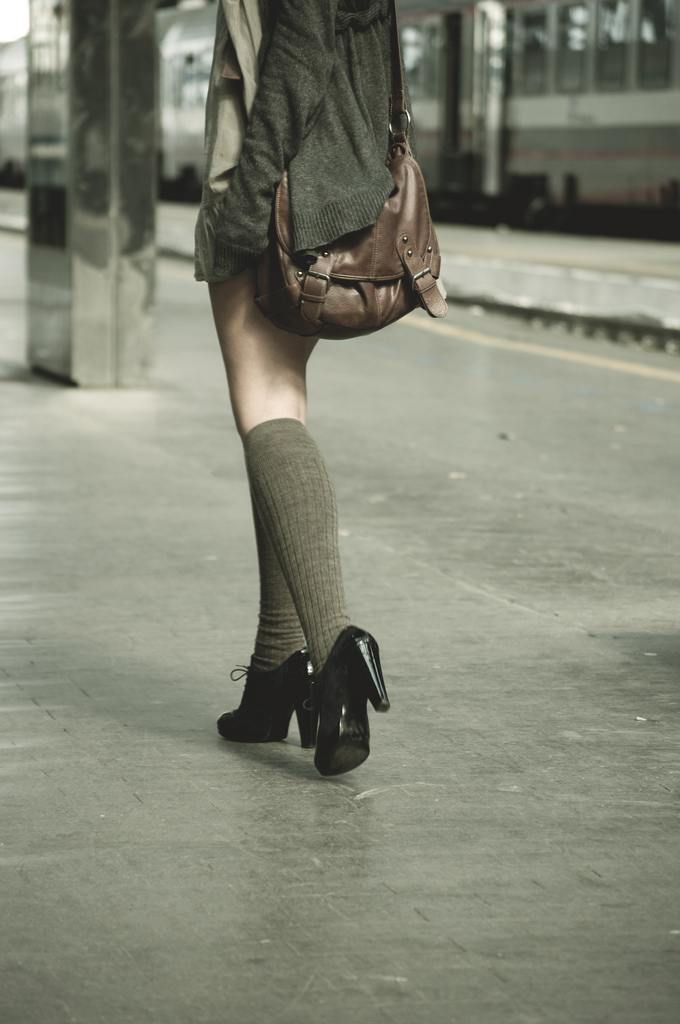 Person with a brown bag and knee-high socks walking at a train station