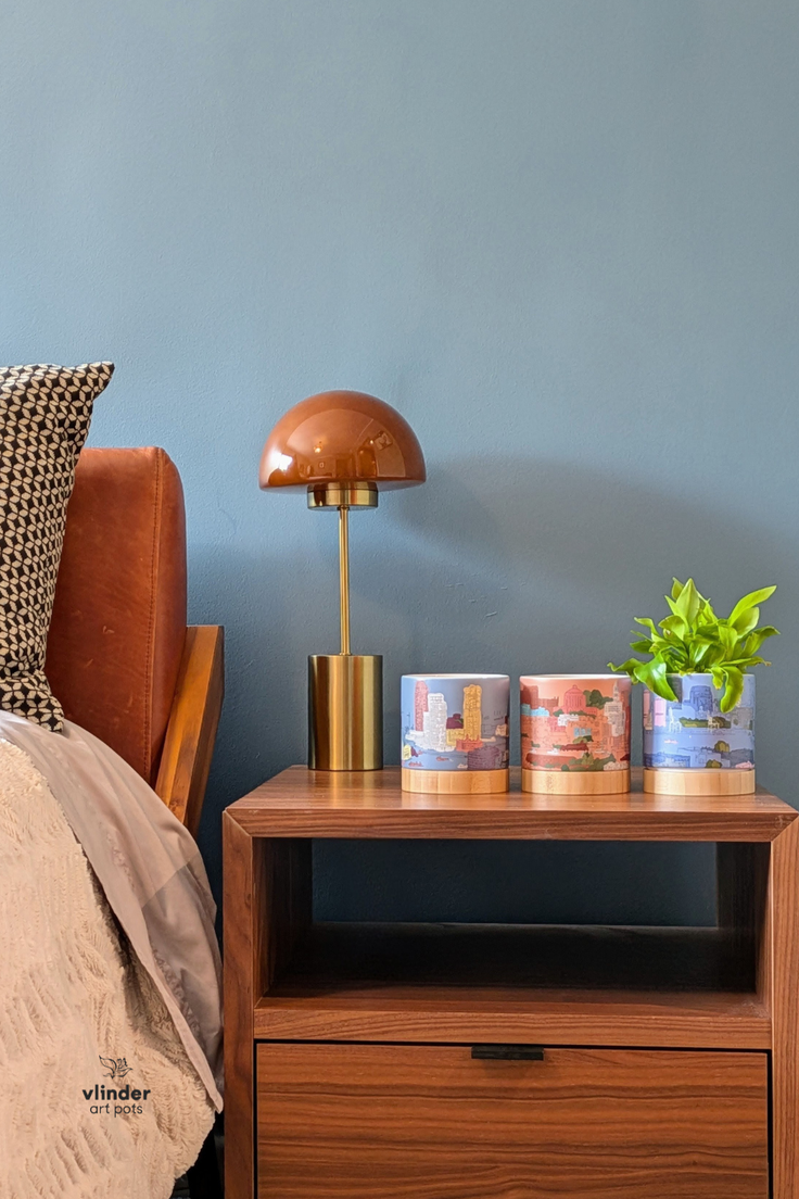 Bedside table with a lamp, three decorative pots, and a plant against a blue wall