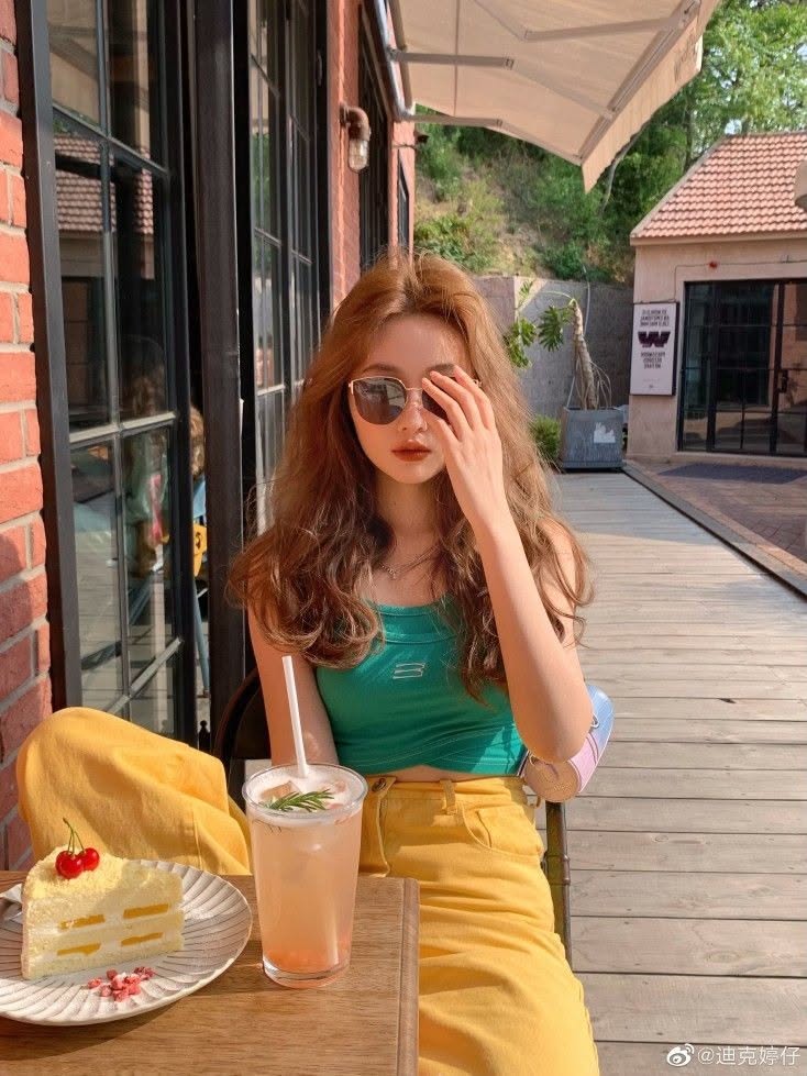 Woman with long wavy hair and sunglasses at an outdoor cafe with cake and a drink