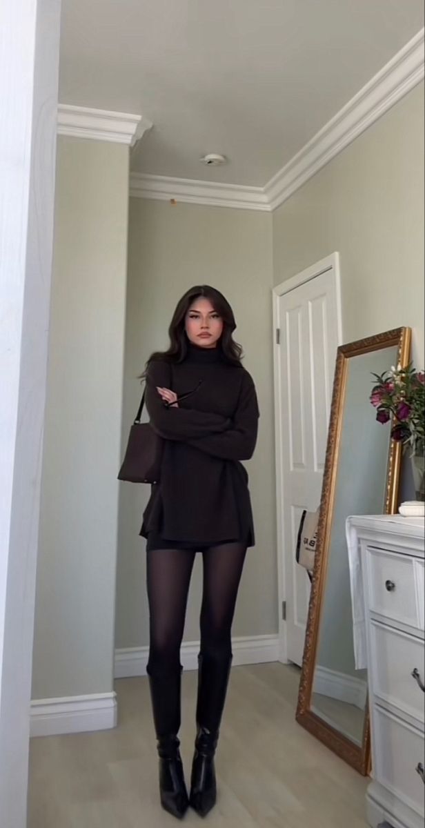 Woman in a dark turtleneck sweater and black tights standing indoors