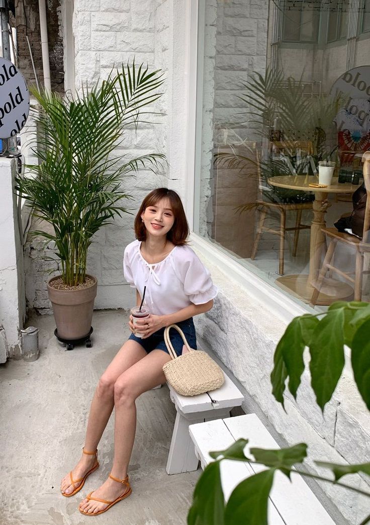 Smiling woman in a white blouse and denim shorts sitting outside a cafe