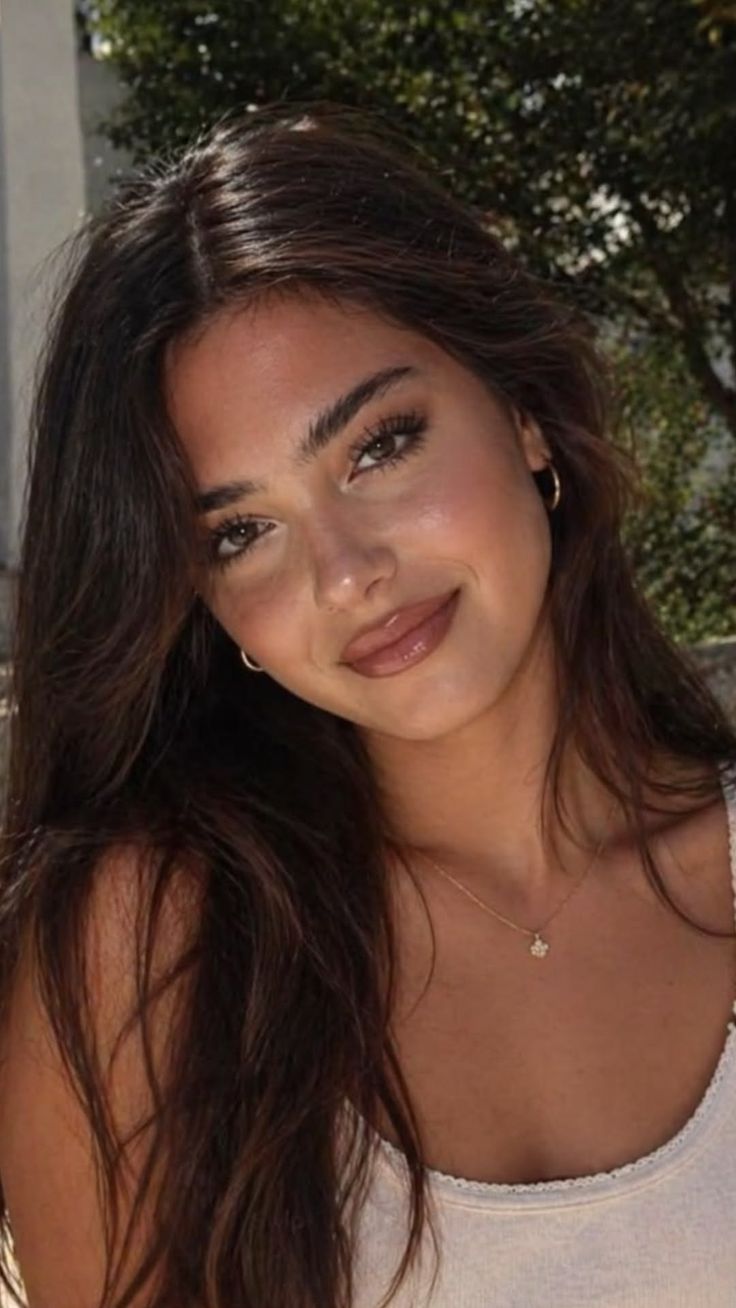 Woman with long dark hair and hoop earrings smiling outdoors