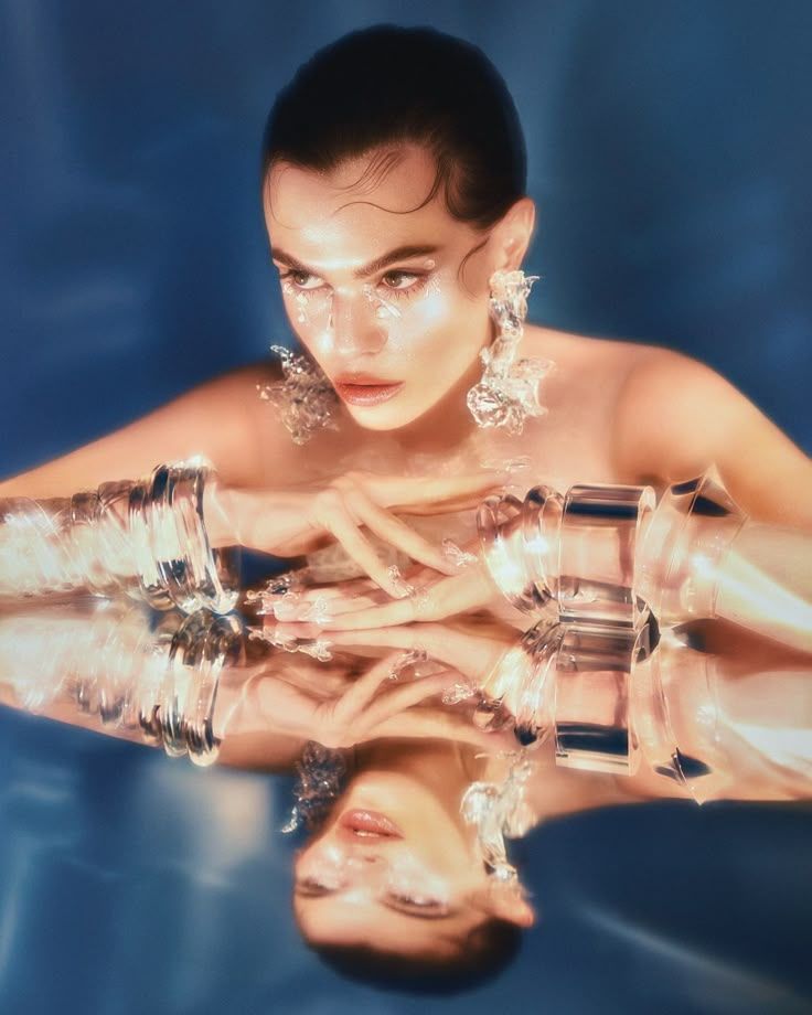 Woman with slicked back hair and clear jewelry reflected on a surface