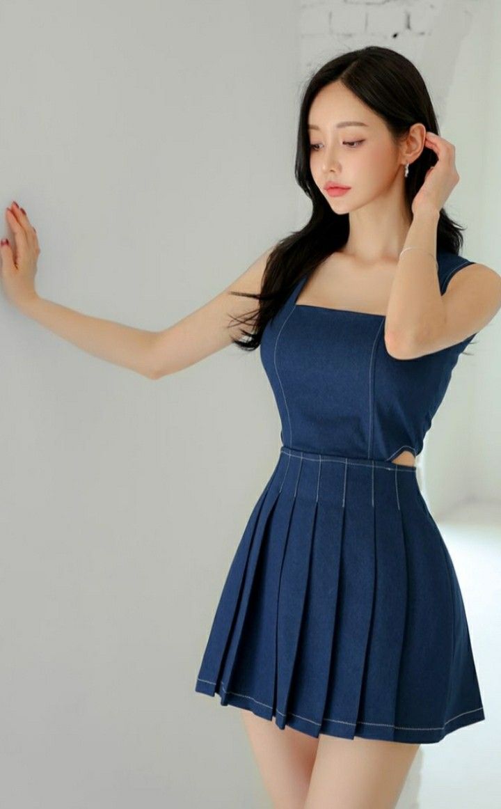 Woman in a blue denim dress with a pleated skirt posing indoors