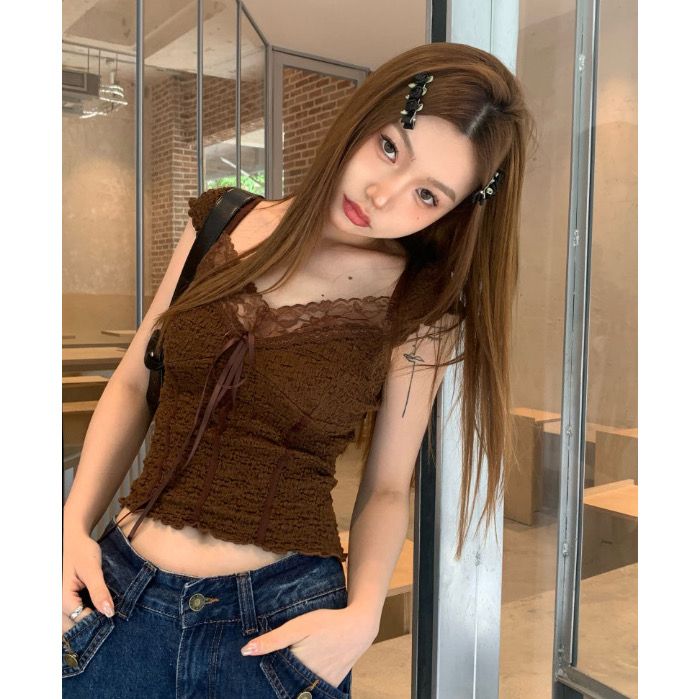 Woman with long brown hair wearing a brown lace-trimmed top and denim jeans indoors