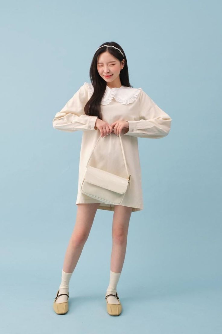 Woman in a white dress with a ruffle collar and headband holding a shoulder bag