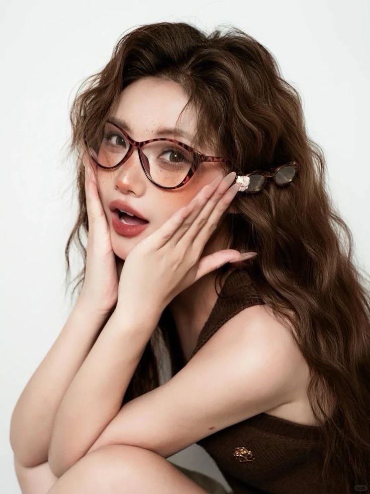 Woman with long wavy hair and glasses posing against a white background