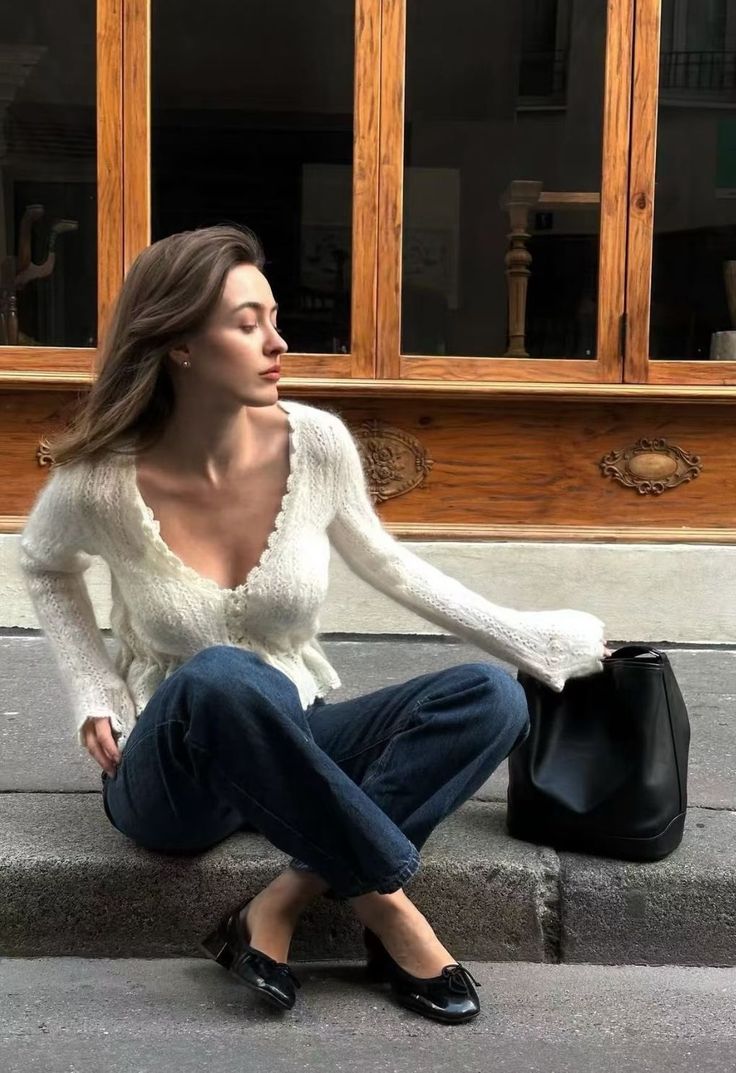 Woman in a white cardigan and blue jeans sitting outdoors